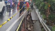 Petugas Satgas memasang terpal biru dan rambu peringatan di lokasi trotoar Jalan Raya Bogor Depok yang longsor akibat hujan deras.