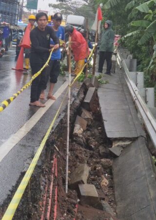 Petugas Satgas memasang terpal biru dan rambu peringatan di lokasi trotoar Jalan Raya Bogor Depok yang longsor akibat hujan deras.
